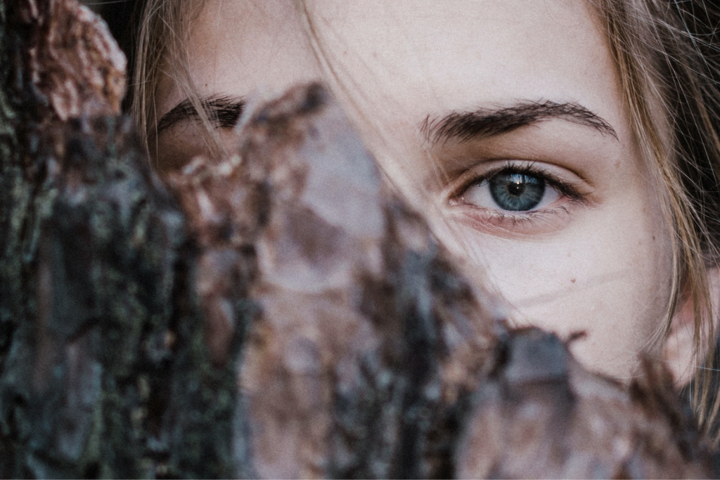 A woman looking to the camera and hiding half of her face behind a tree for a real sense of identity