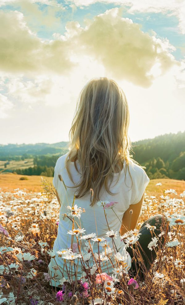 A woman laying in a bed of flowers looking at her life from the outside