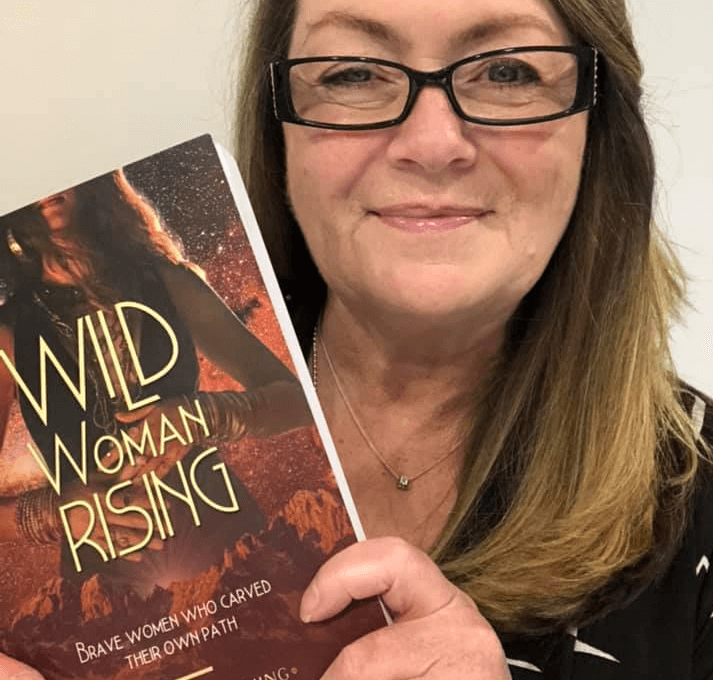 Debra J Hicks holding a copy of the joint co author book she published Wild Woman Rising